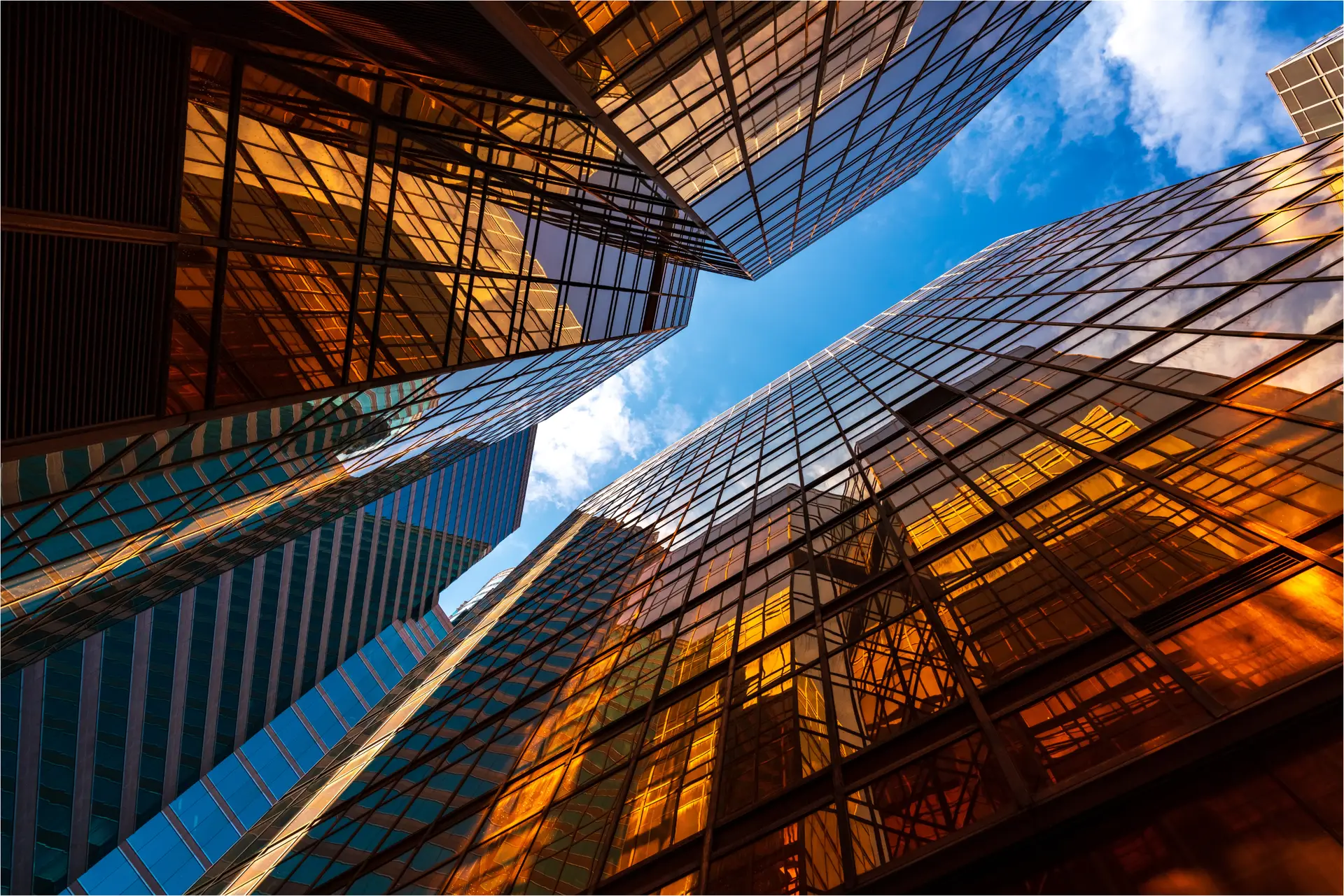 Ground view looking up at glass buildings reflecting the sky in a cityscape.