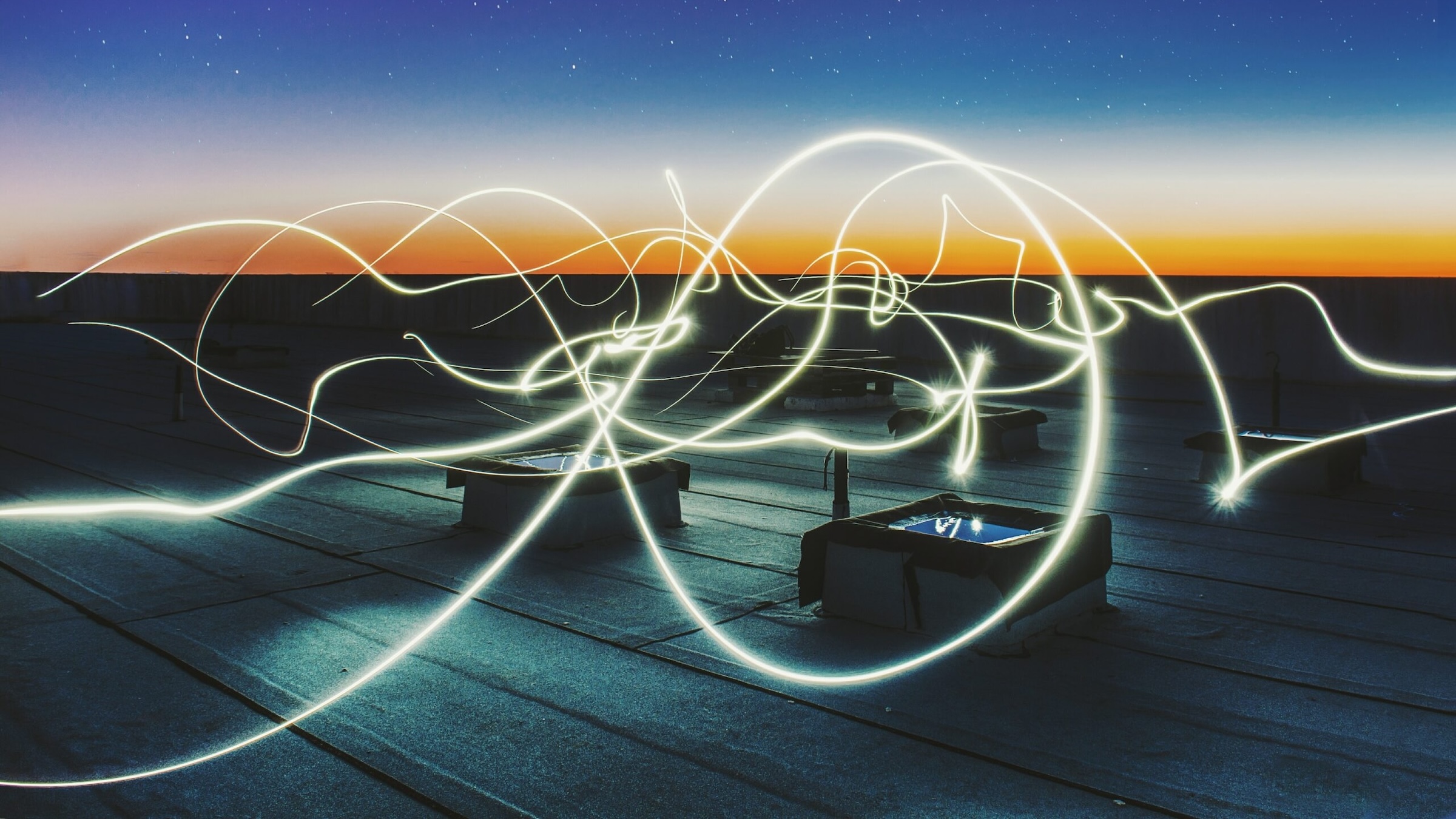 Light streaks swirling over a rooftop at sunset with a clear, starry sky.