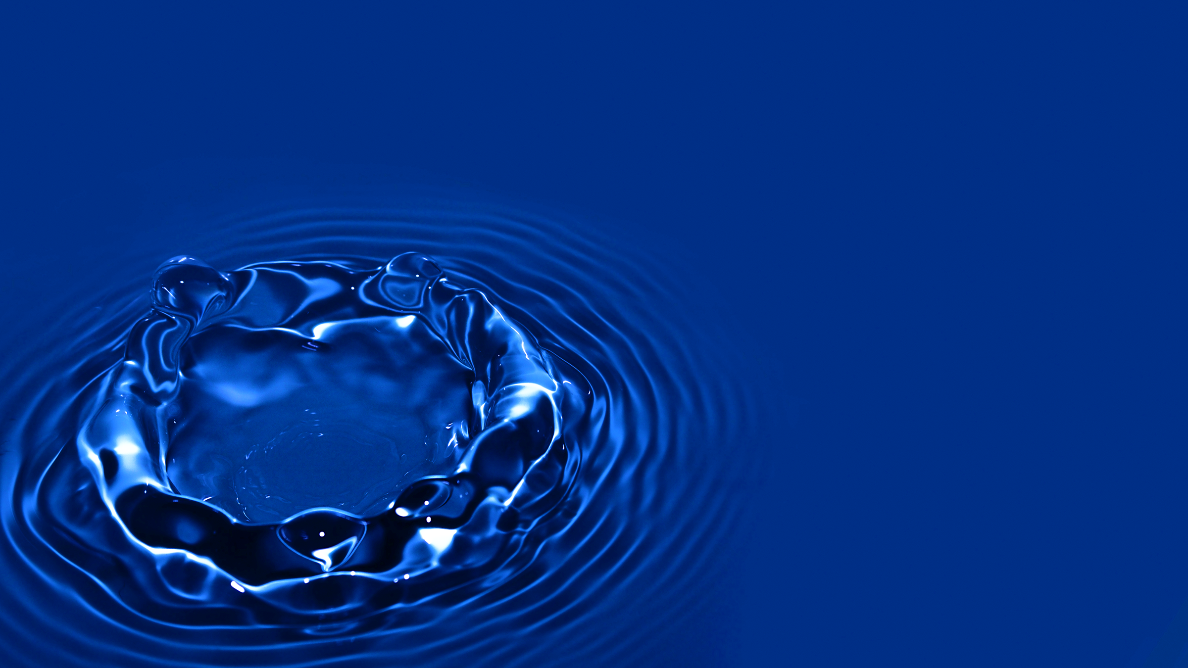 Vivid blue water droplet creating 3D ripples on a liquid surface.